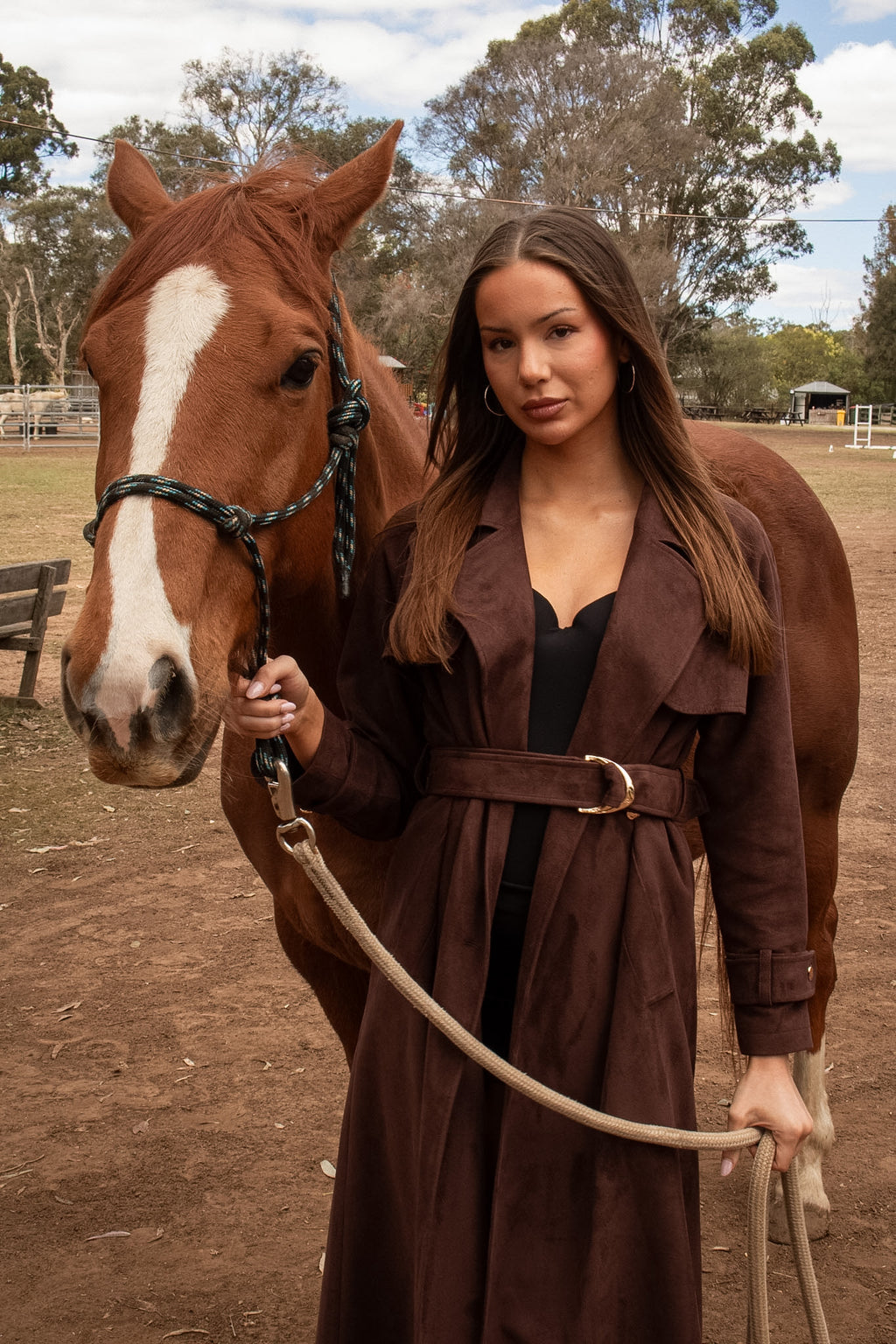 Front view of the Flora Trench in espresso suede with a belted waist, modelled beside a horse